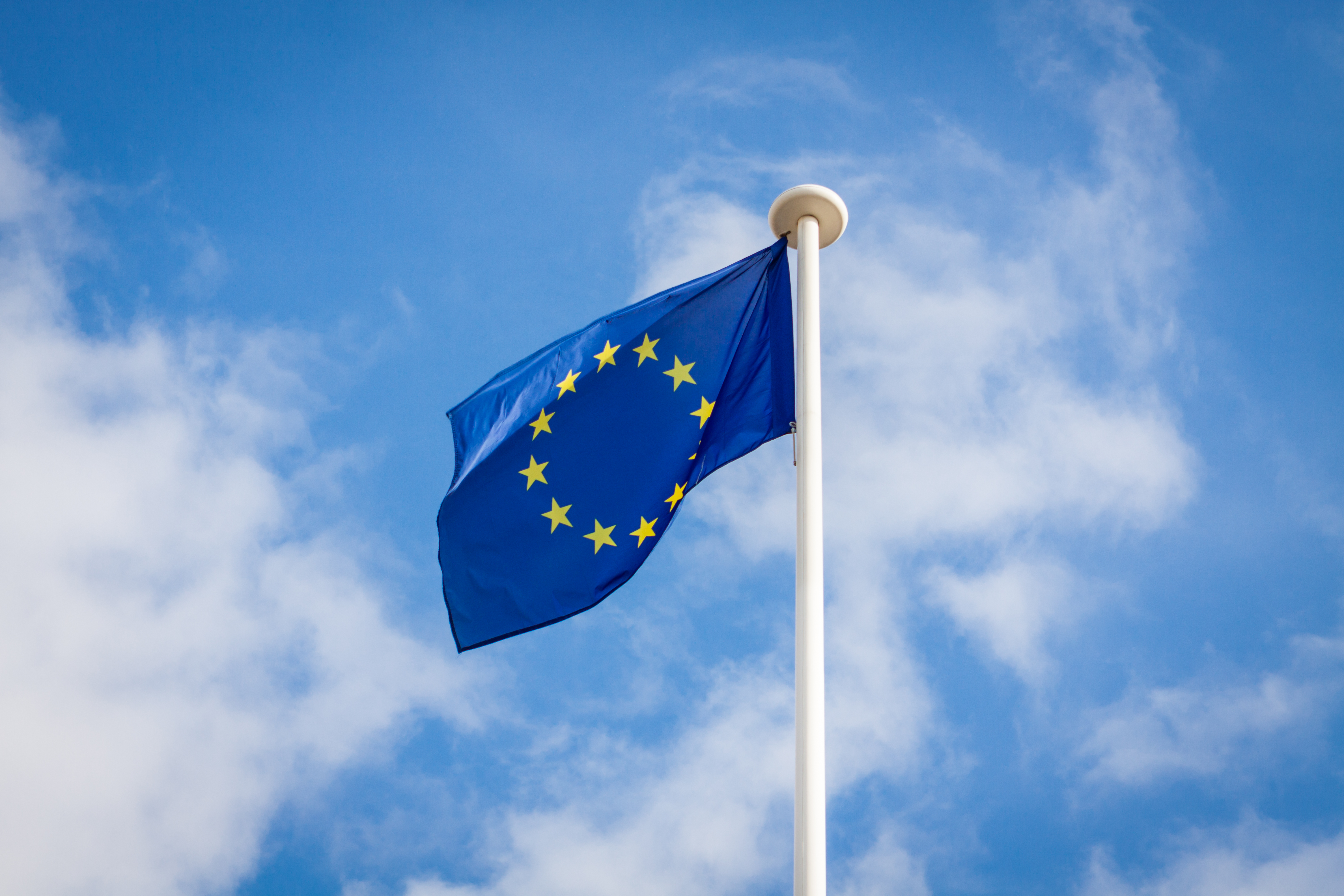The fluttering flag of European Union on a pole, with a blue sky with white clouds in the background